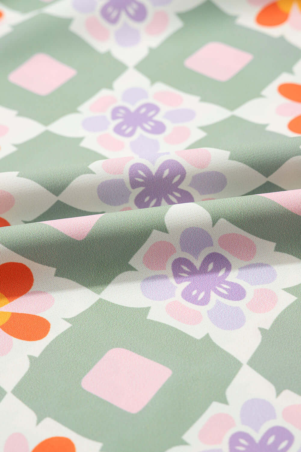 Close-up of mint green fabric with colorful floral geometric pattern in pink, purple, and orange.