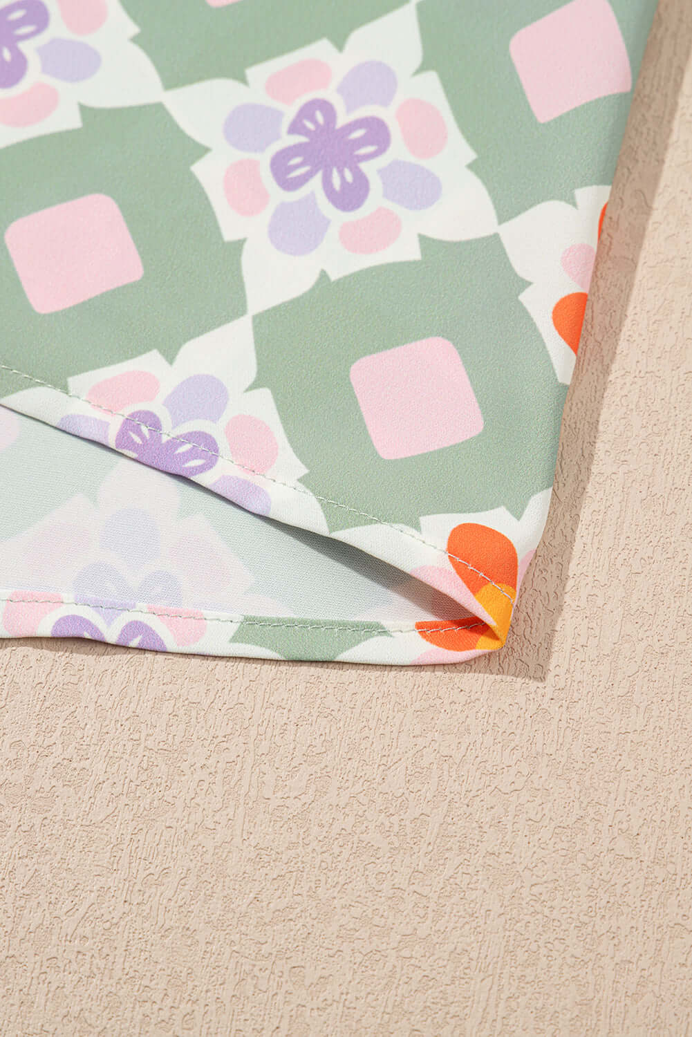 Close-up of mint mosaic dress fabric featuring green geometric floral pattern and vibrant coral accents.