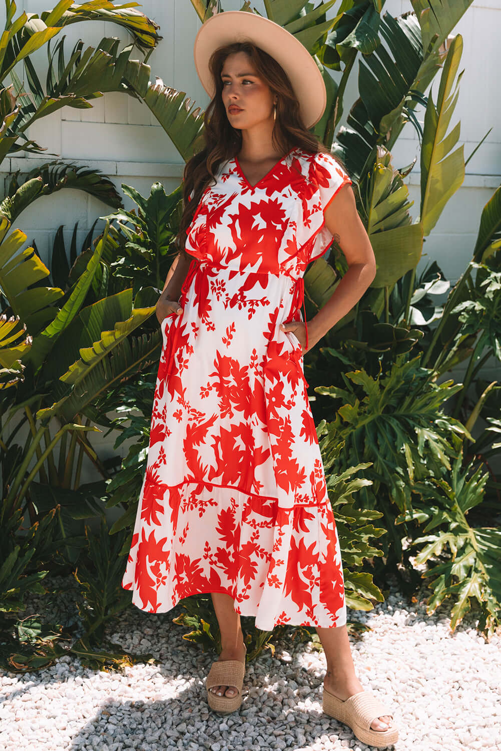 Model wearing the Salsa Garden Dress featuring a red floral print on ivory, surrounded by lush greenery.