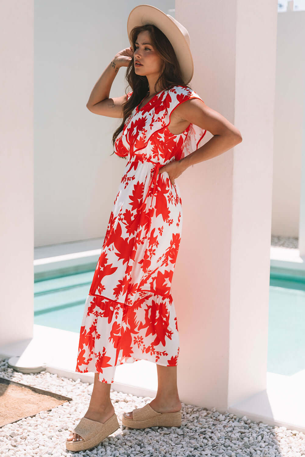 Model wearing a red floral print Salsa Garden Dress by a pool, showcasing a summer style with flutter sleeves and tiered skirt.
