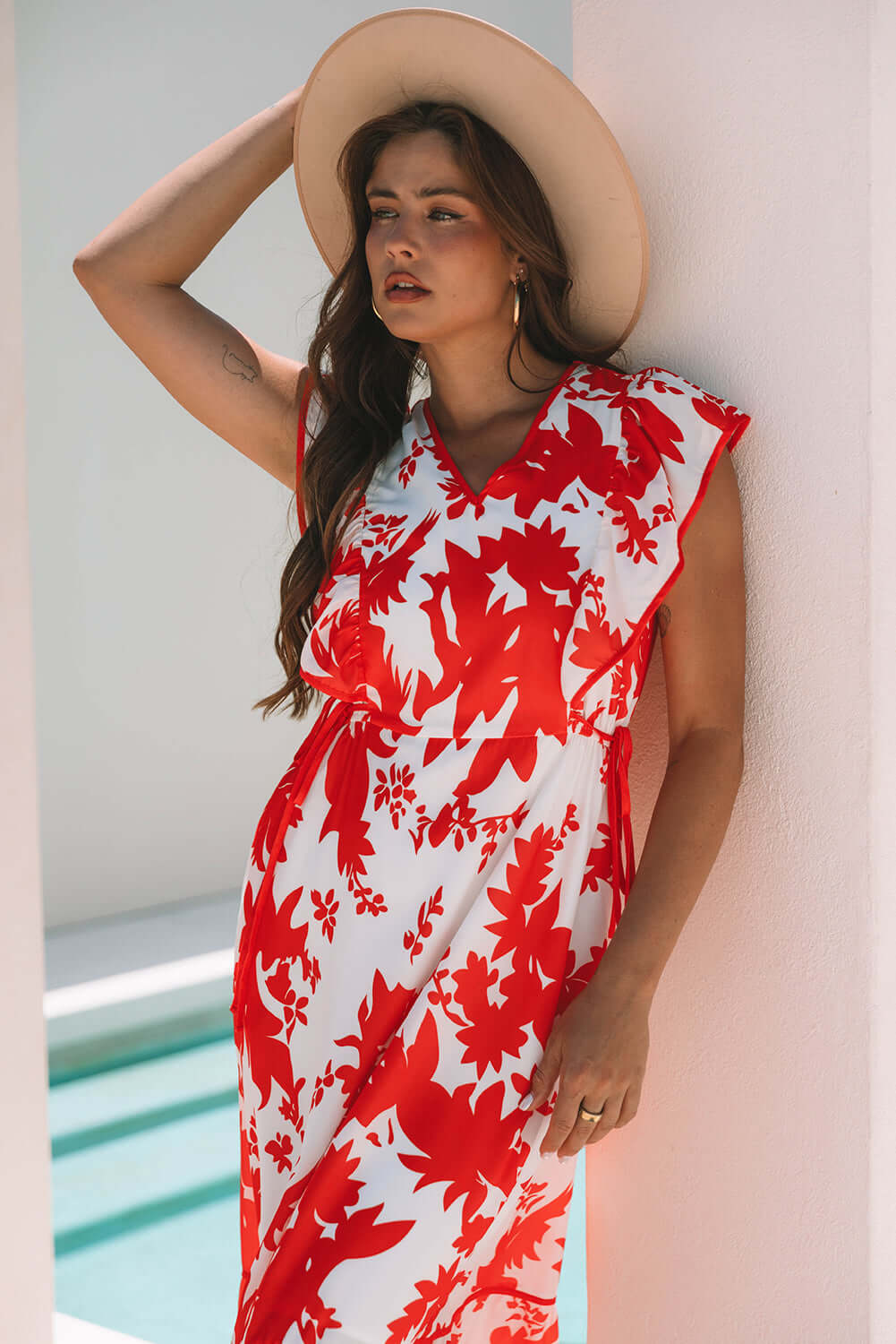 Model wearing a red floral Salsa Garden Dress with flutter sleeves and a wide hat, set against a summer backdrop.