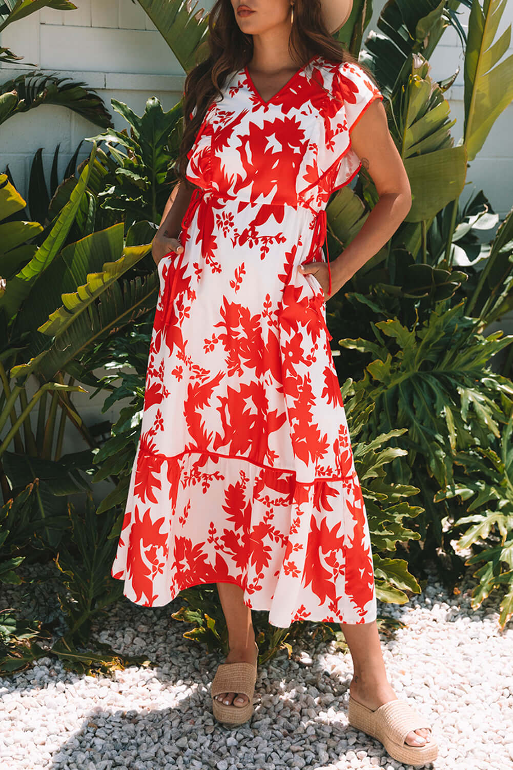 Model wearing the Salsa Garden Dress with red floral print on ivory, surrounded by tropical greenery.