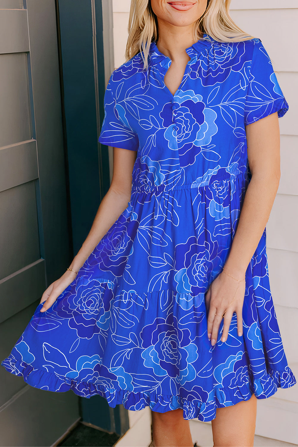 Model wearing a vibrant blue floral dress with a tiered skirt and short sleeves, perfect for casual summer outings.