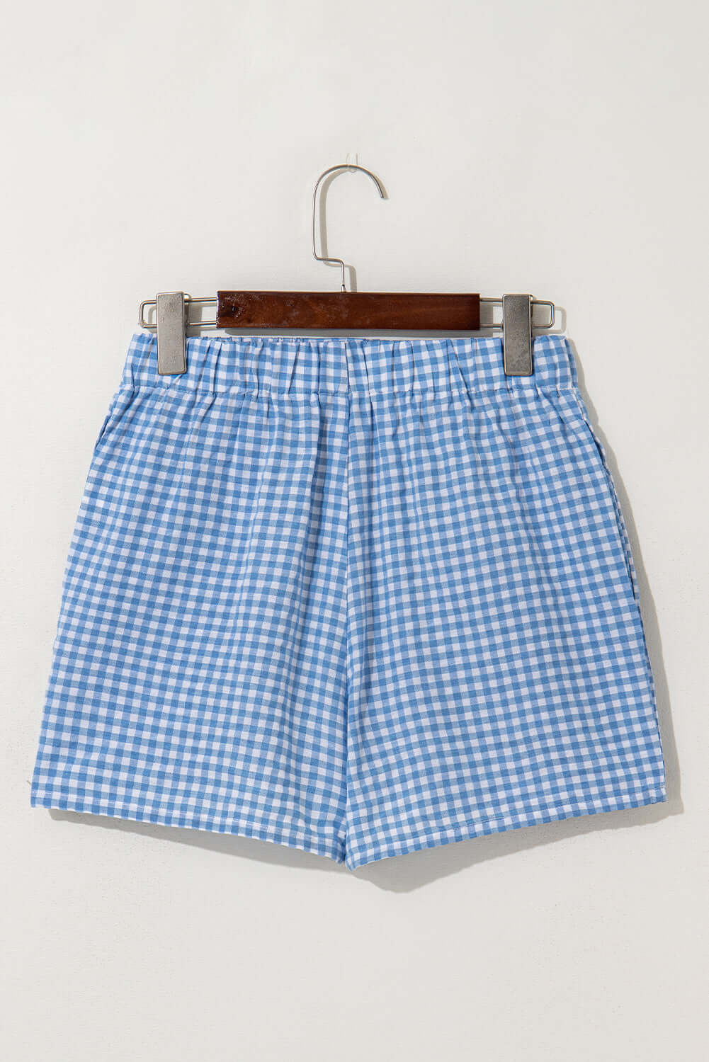Blue gingham high waist shorts hanging on a wooden hanger, ideal for warm-weather picnics and casual outings.