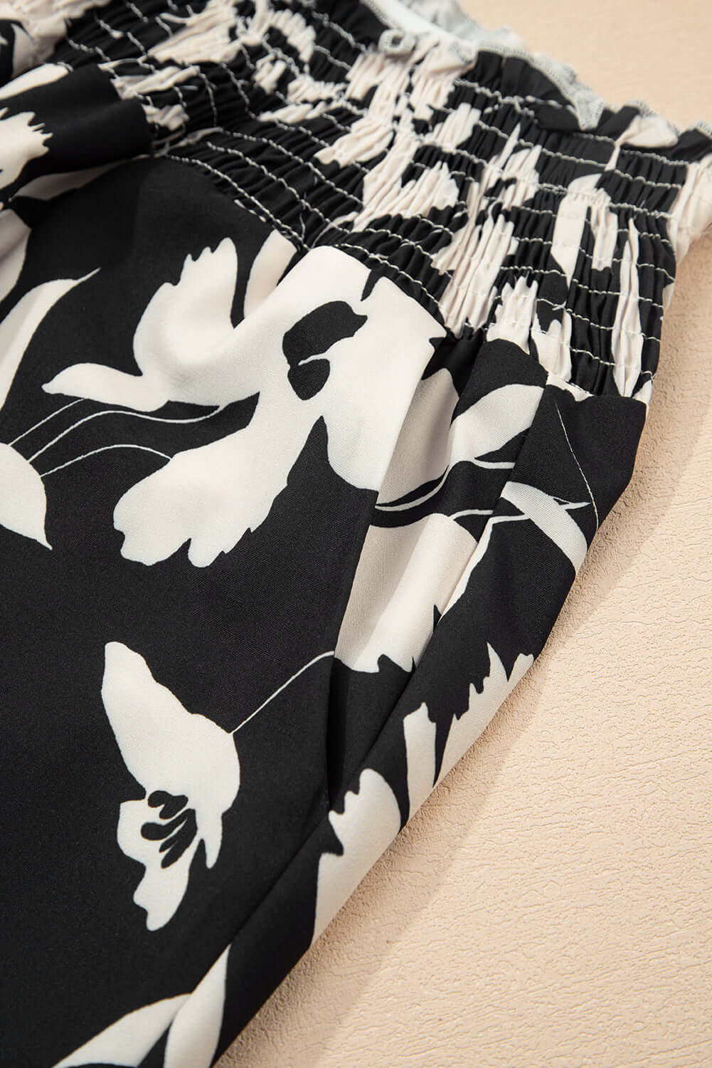 Close-up of EVENING OUT WIDE LEG PANTS showing smocked waist and black floral print design.