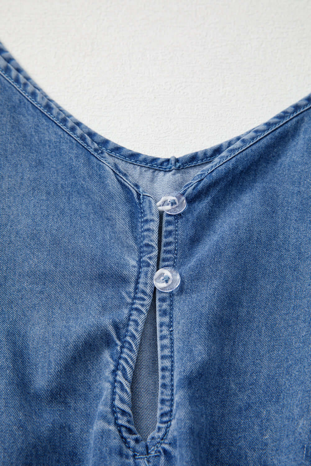 Close-up of the V-neckline and button detail on the Shore Thing Denim Romper in medium blue wash.