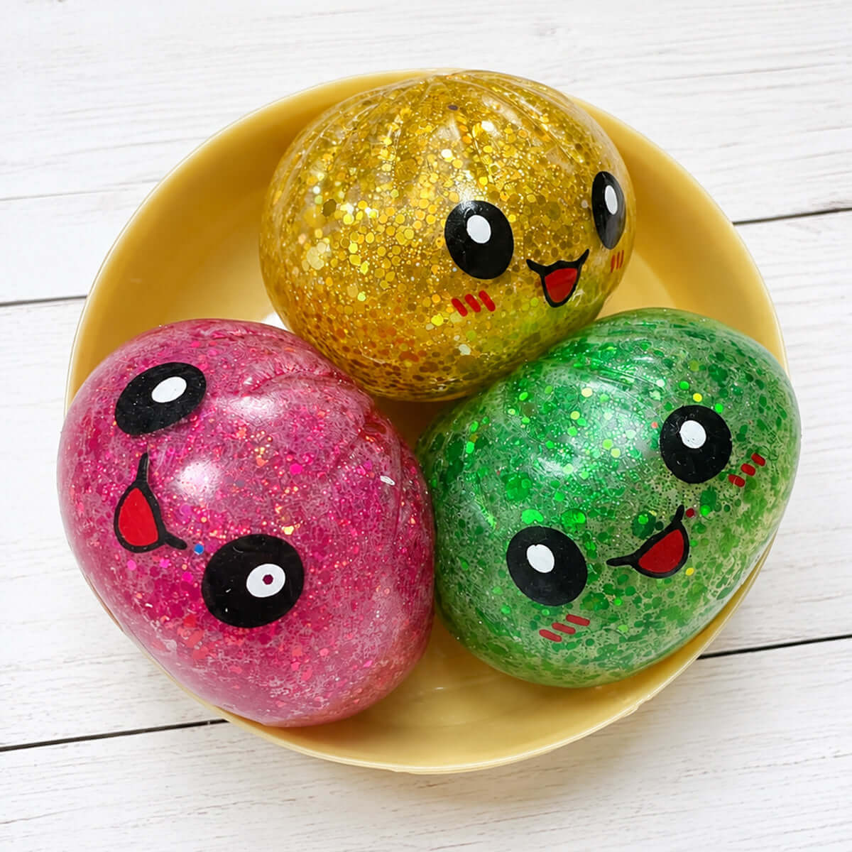 Three colorful Glitter Orbeez Dumpling Trio squishy toys in a bowl, featuring pink, green, and gold glittery designs.