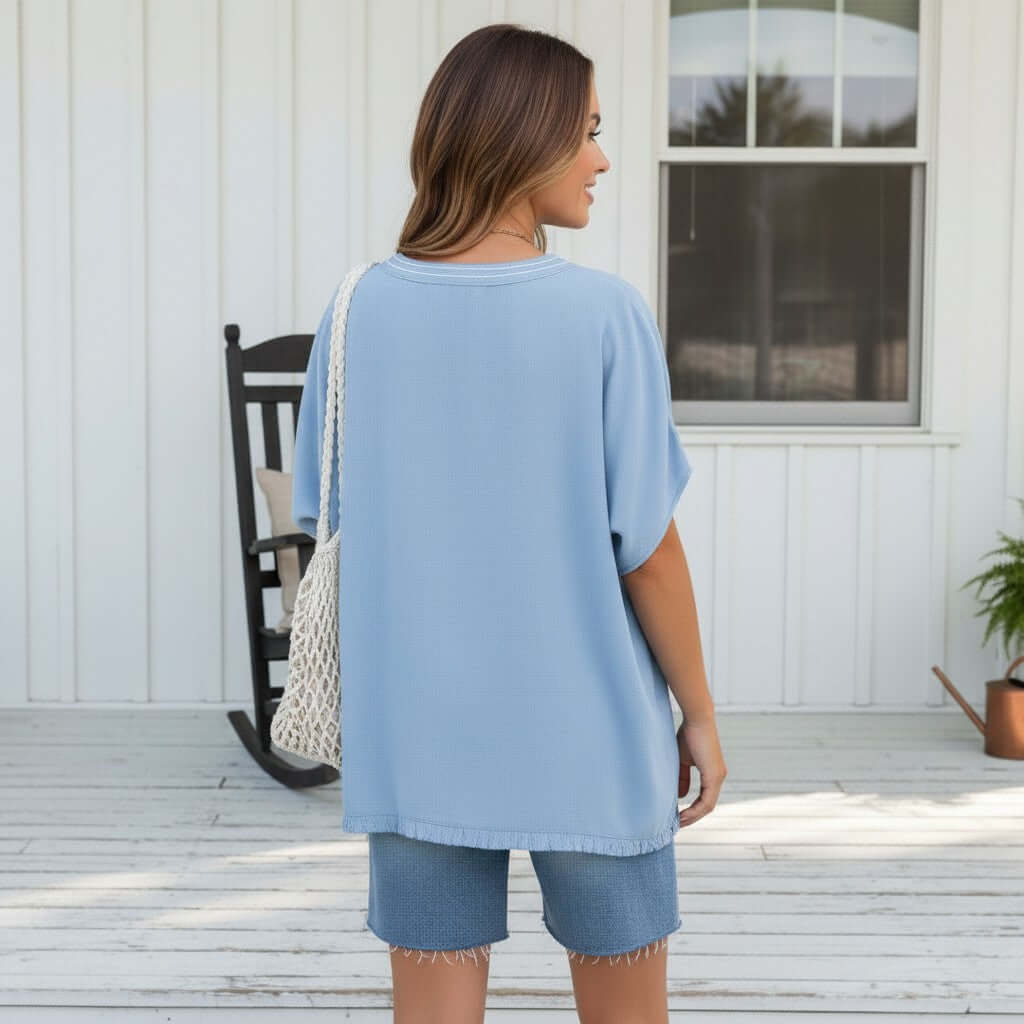 Woman wearing the COASTAL DAYDREAMS TOP - GIgio with blue shorts and a tote bag, standing on a porch.