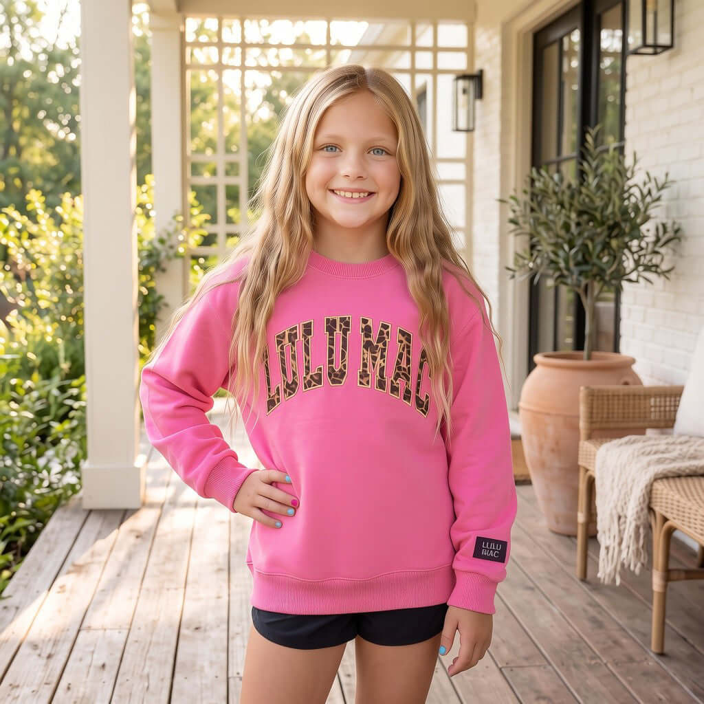 Girl wearing LULU MAC YOUTH TAFFY W/ LEOPARD crewneck in bright pink in a cozy outdoor setting.