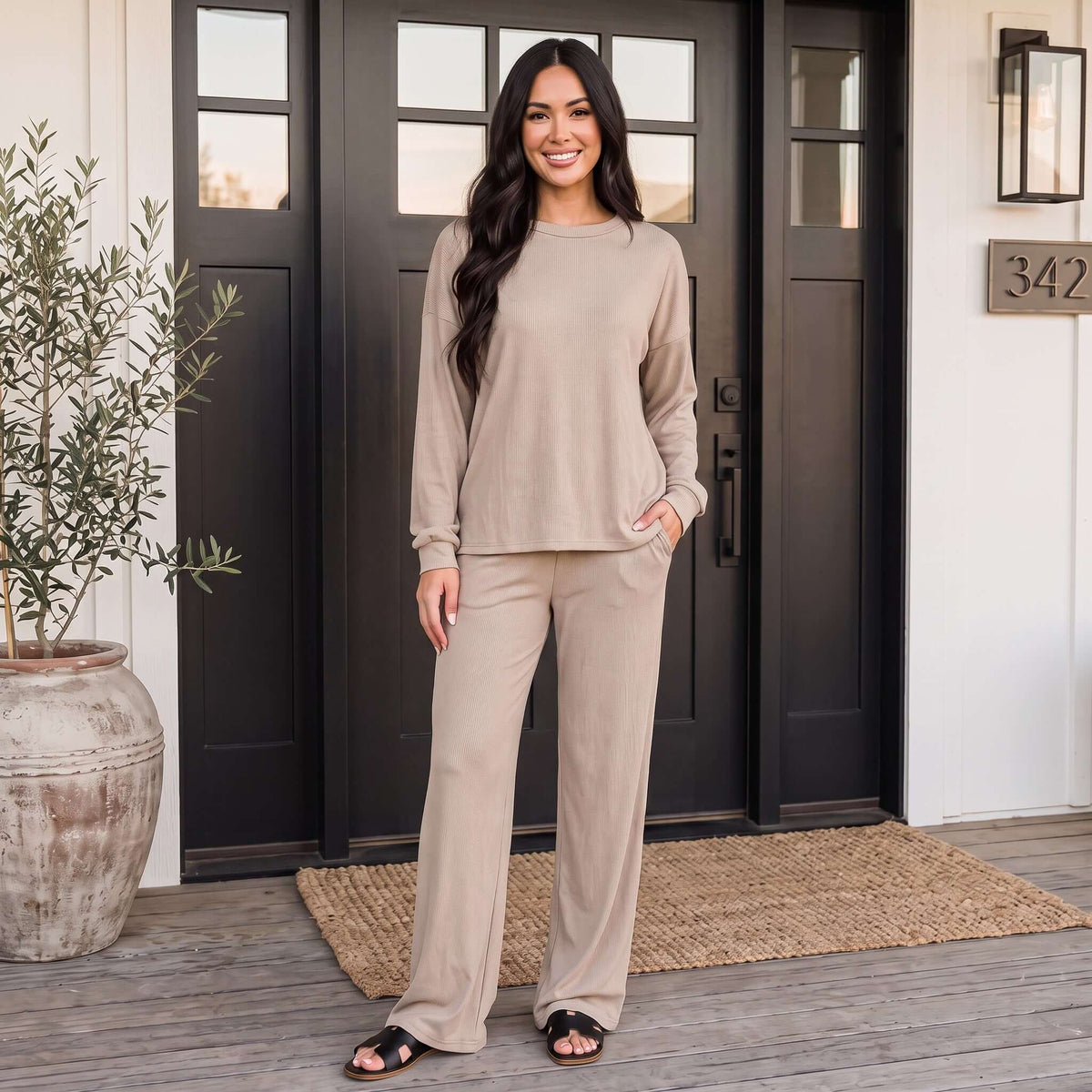 Model wearing SOFT LIFE PANTS SET (2 colors) in soft beige, standing at a modern entryway.