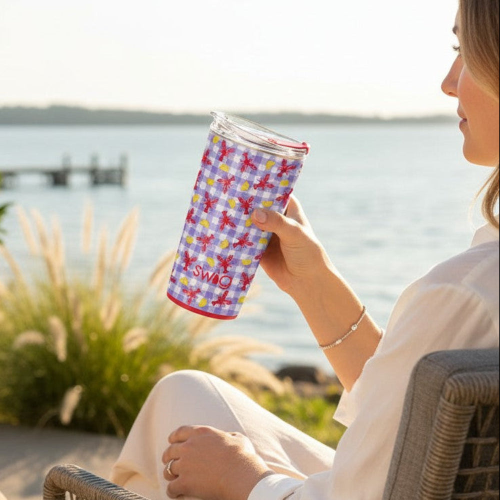 LET THE GOOD TIMES BOIL - 22 OZ TRAVEL MUG - Swig held by a woman by the lakeside in a vibrant design.
