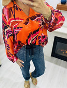Woman wearing LAVA LUXE BLOUSE - JODIFL in vibrant orange and pink, styled with casual jeans and sandals.