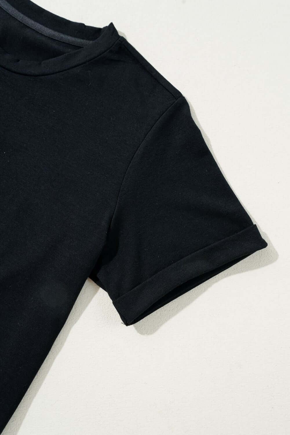 Close-up of a black t-shirt sleeve, showcasing soft cotton blend fabric and rolled cuffs.