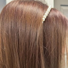 Close-up of a pearl embellished hairband worn on long brown hair, adding elegance and sophistication to the look.