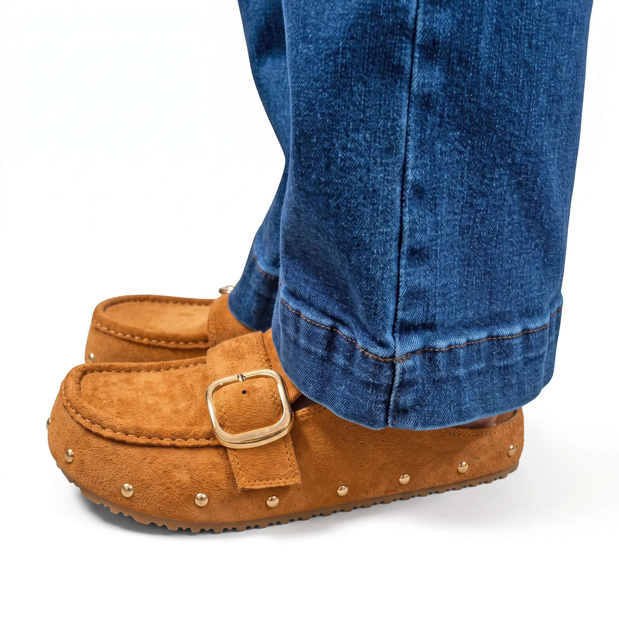 CIDER SEASON SLIP-ONS in warm suede color, styled with denim pants, featuring a metal buckle detail and stud accents.