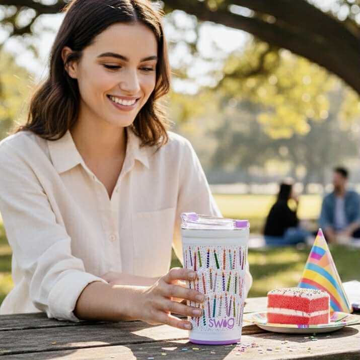 A woman enjoying the MAKE A WISH 24 oz - SWIG tumbler in a park during a celebration.