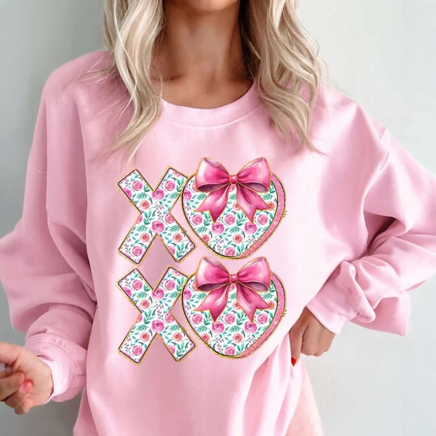 LOVE YOU MORE CREWNECK featuring XOXO floral print bows on cozy pink fabric, perfect for Valentine’s Day.