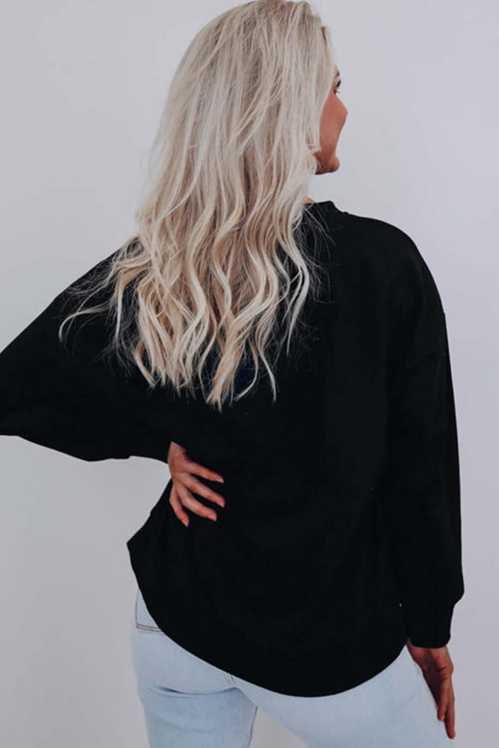 Back view of a woman wearing a black MERRY & BRIGHT SWEATER by Vivian-Lu, showcasing its relaxed fit.