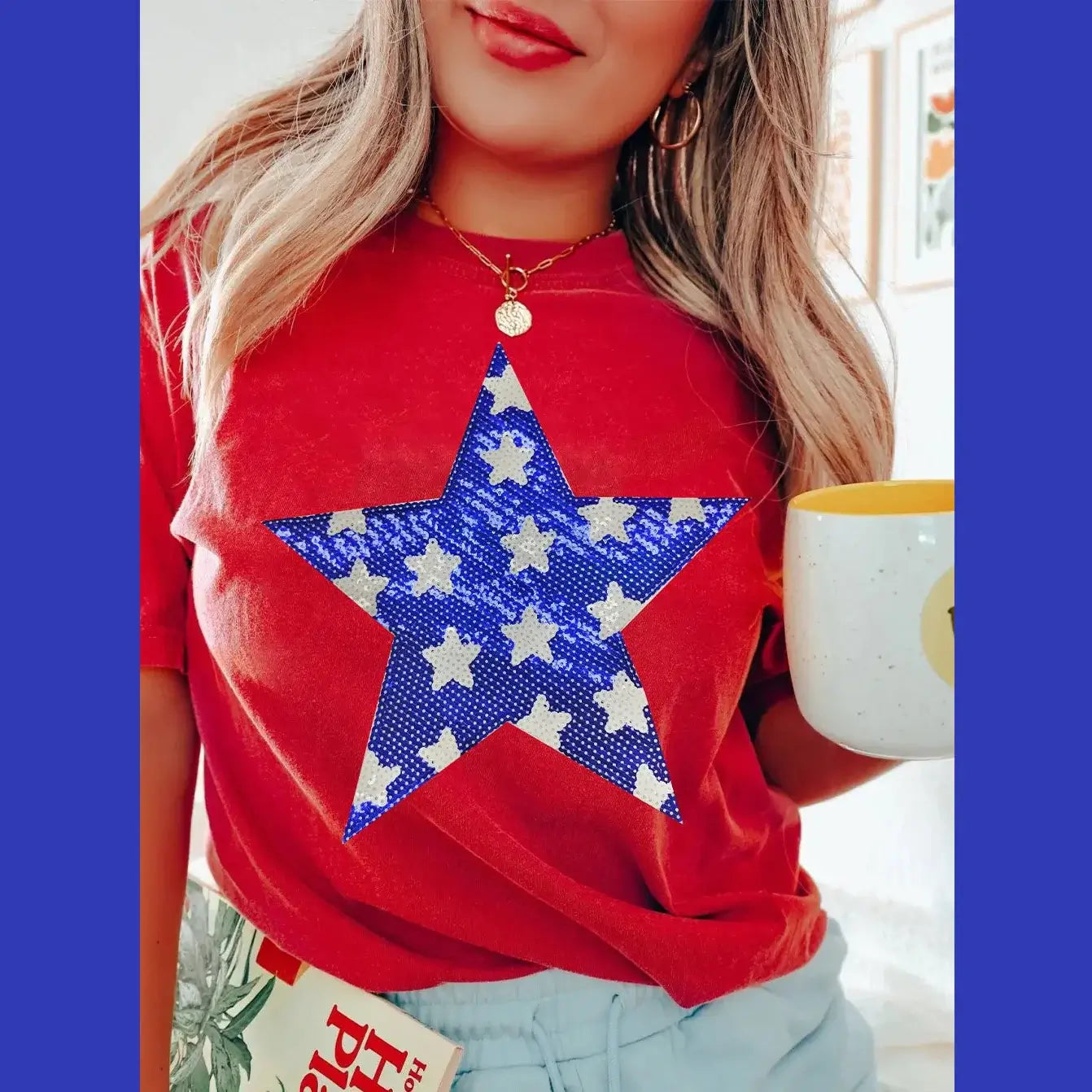 Woman in red Sequin Starlet Tee with blue star graphic, holding a coffee cup, styled for casual comfort.