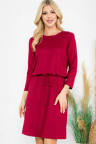 Model wearing a red Wine and Dine Dress with 3/4 sleeves, cinched waist, and pockets, showcasing a stylish knee-length design.
