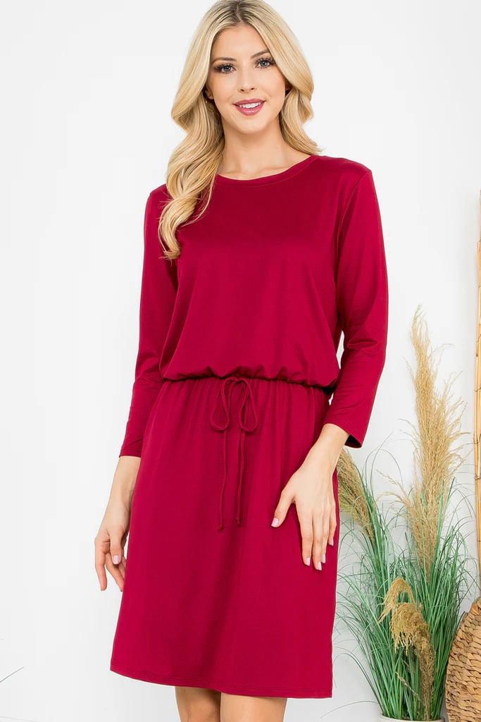 Model wearing a red Wine and Dine Dress with 3/4 sleeves, cinched waist, and pockets, showcasing a stylish knee-length design.