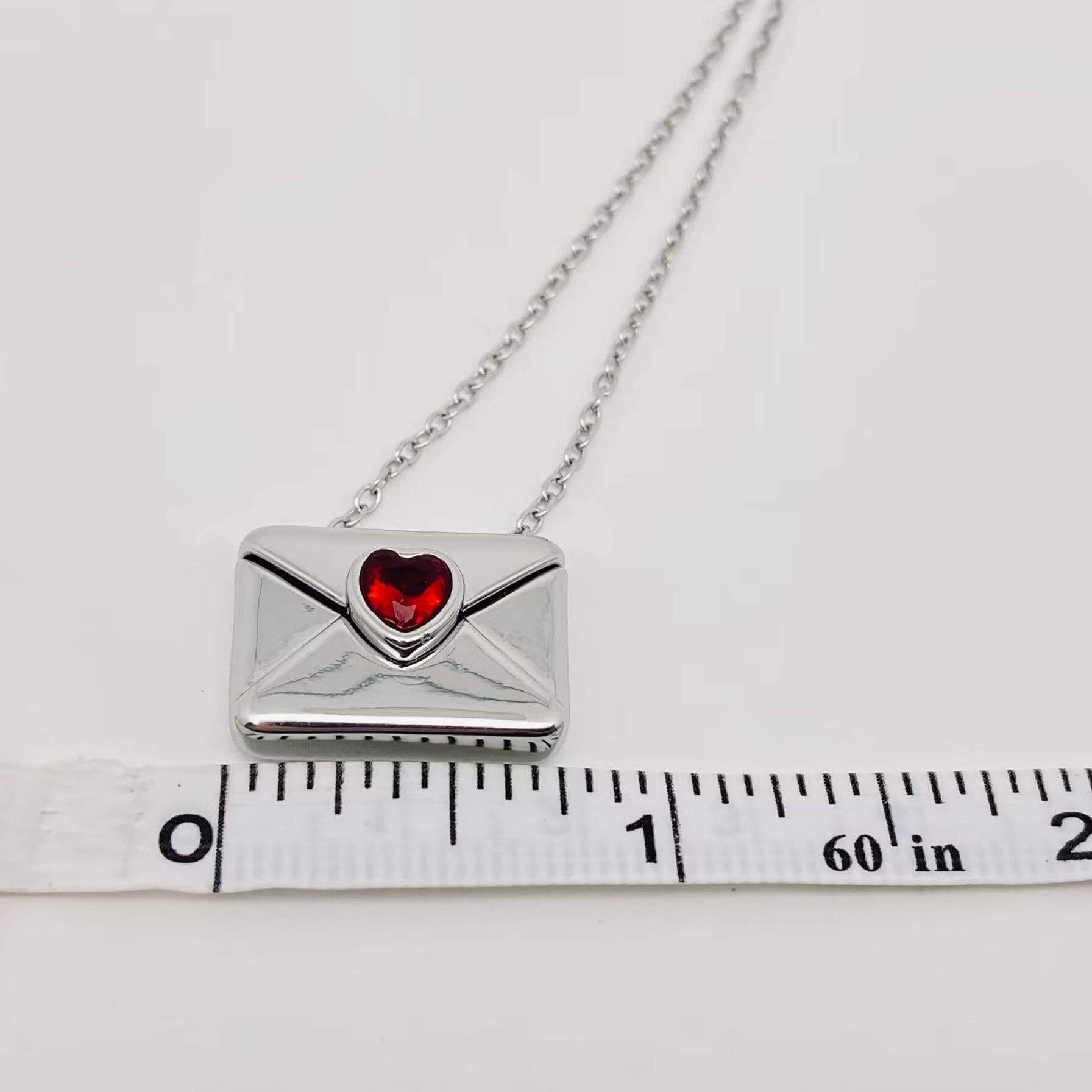 LOVE LETTER NECKLACE featuring a silver envelope pendant with a red heart-shaped stone, perfect for meaningful gifting.