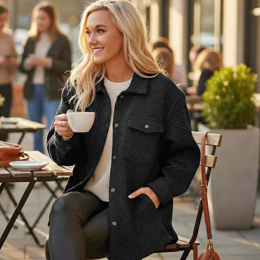 Model wearing WARM IMPRESSIONS BUTTON DOWN shacket while enjoying coffee at a cafe, showcasing cozy style.