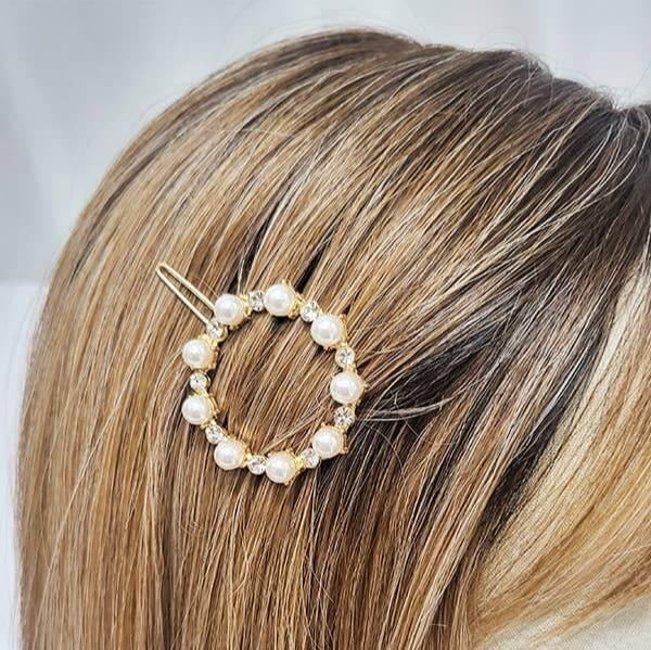 Gold tone barrette adorned with faux pearls, featuring a round design on blonde hair.
