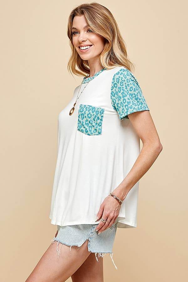 Woman wearing SPOT OF STYLE TEE with turquoise leopard print sleeves and pocket, styled casually with shorts.