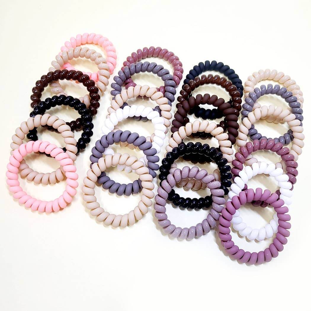 Colorful assortment of Twist & Tell hair ties in neutral tones and pink, showcasing 6-piece coil band set.