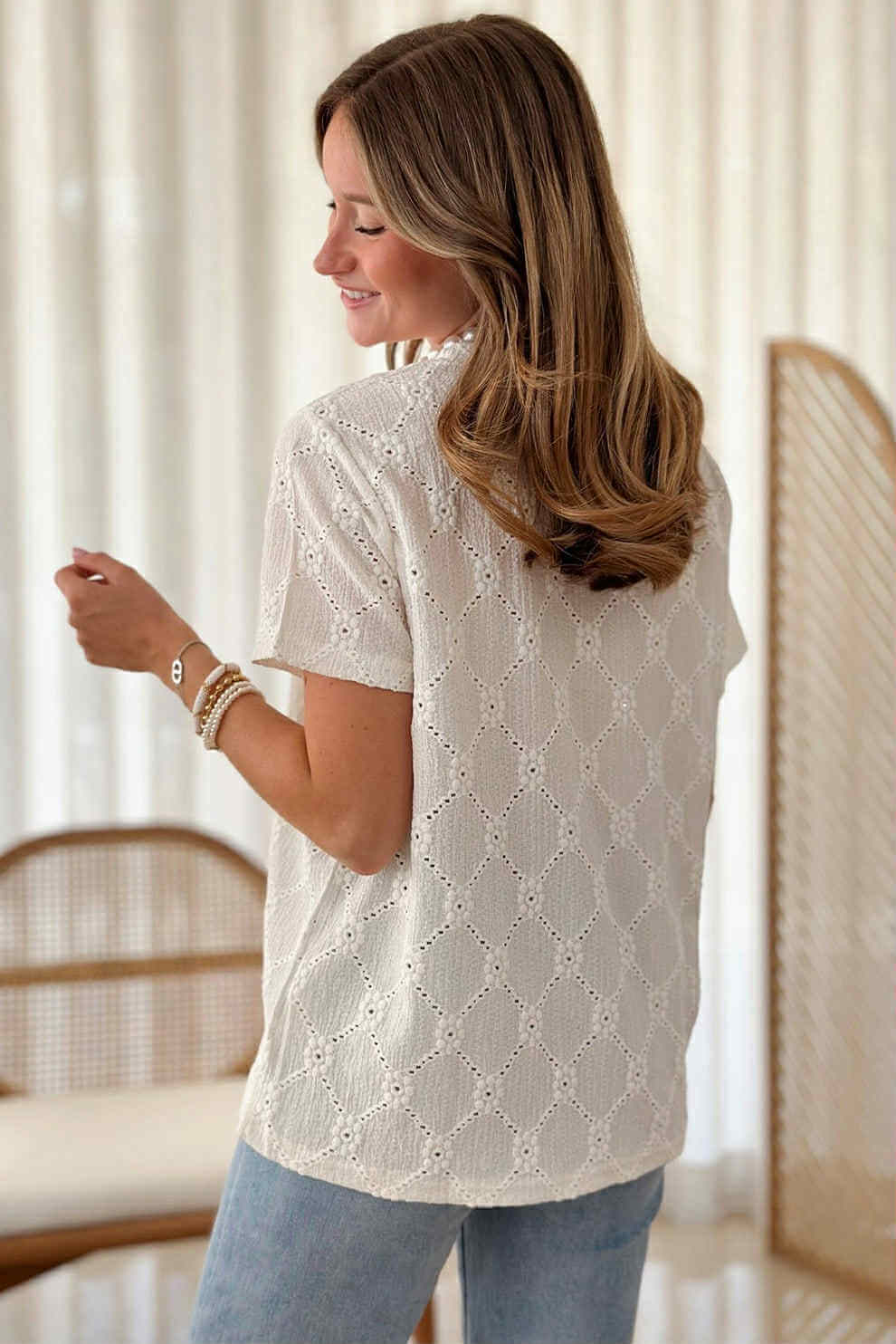 Back view of a woman wearing a Lace Grace Top with intricate eyelet embroidery in ivory.