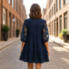 Woman wearing DEEP SEA DREAMS DRESS Umgee, showcasing the navy tiered design and floral sleeves in an urban setting.
