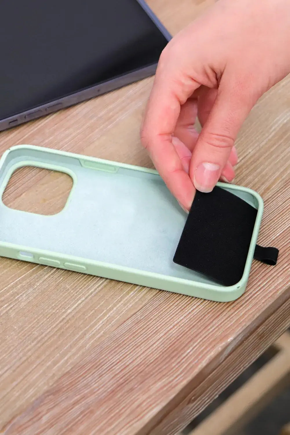 Hand removing black pouch from mint green Hands-Free Harmony Crossbody phone case on a wooden surface.