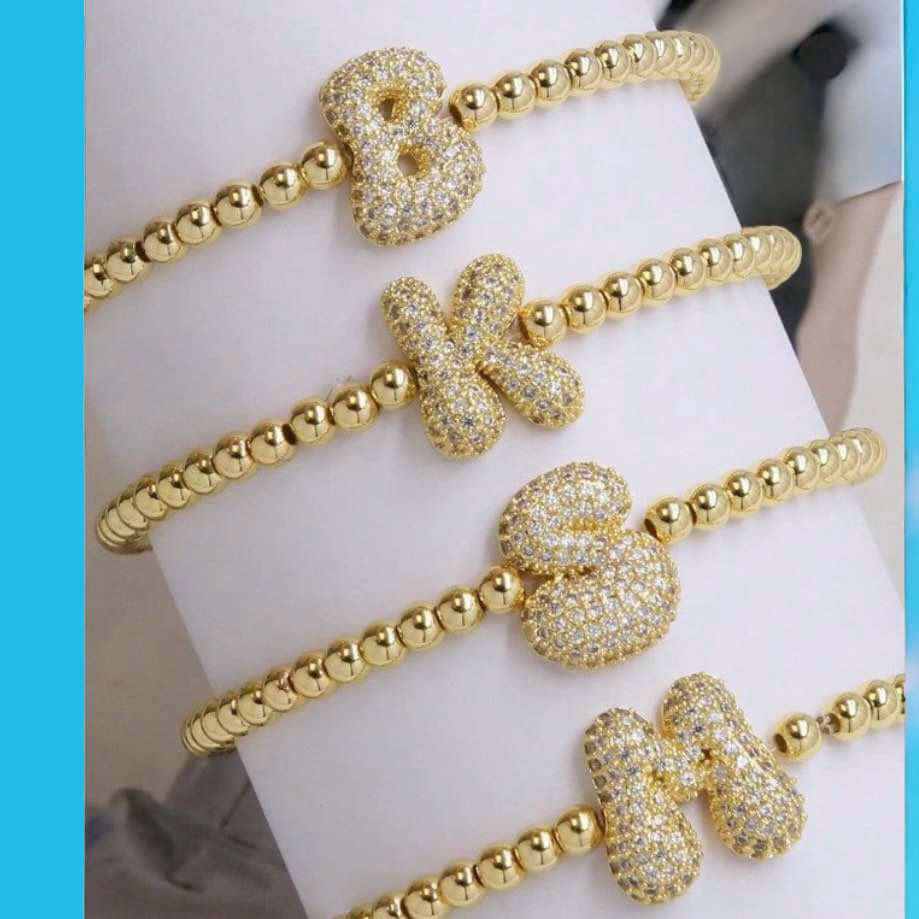 Golden rhinestone letter bracelets with initials B, K, S, and M on a stretchy beaded band for personalized glam.