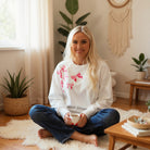 Woman in a cozy setting wearing the DARLING DETAILS TOP with sequin bowknot design, enjoying a cup of tea.