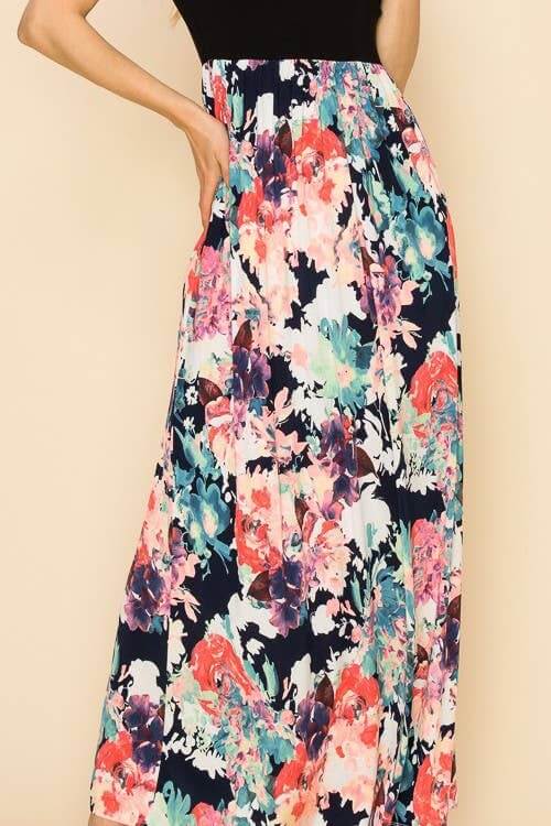 Woman wearing the Raven Radiance Maxi Dress with a black bodice and vibrant watercolor floral skirt.