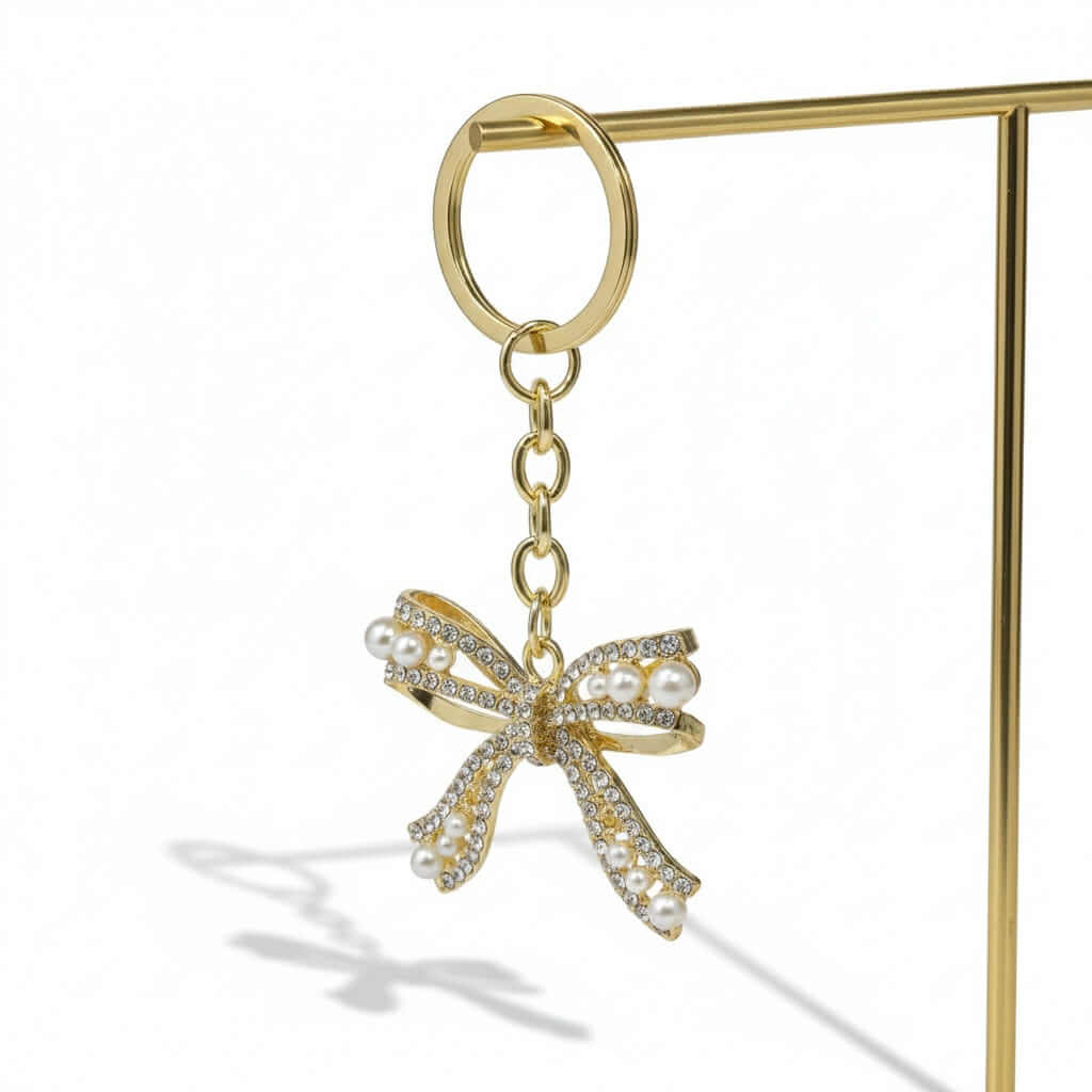 ENCHANTED BOW Bag Charm / Keychain with rhinestones and faux pearls in gold tone on display.