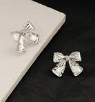 SILVER BOW Stud Earrings from Vivian-Lu collection, showcasing elegant design on a textured surface.