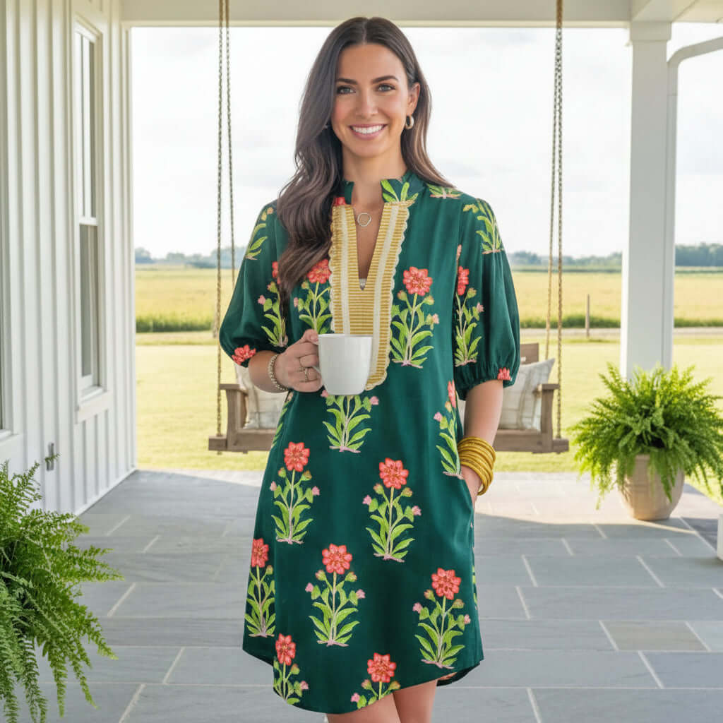 Model wearing RADIATE CONFIDENCE DRESS with pockets, showcasing floral print and relaxed silhouette, holding a cup.