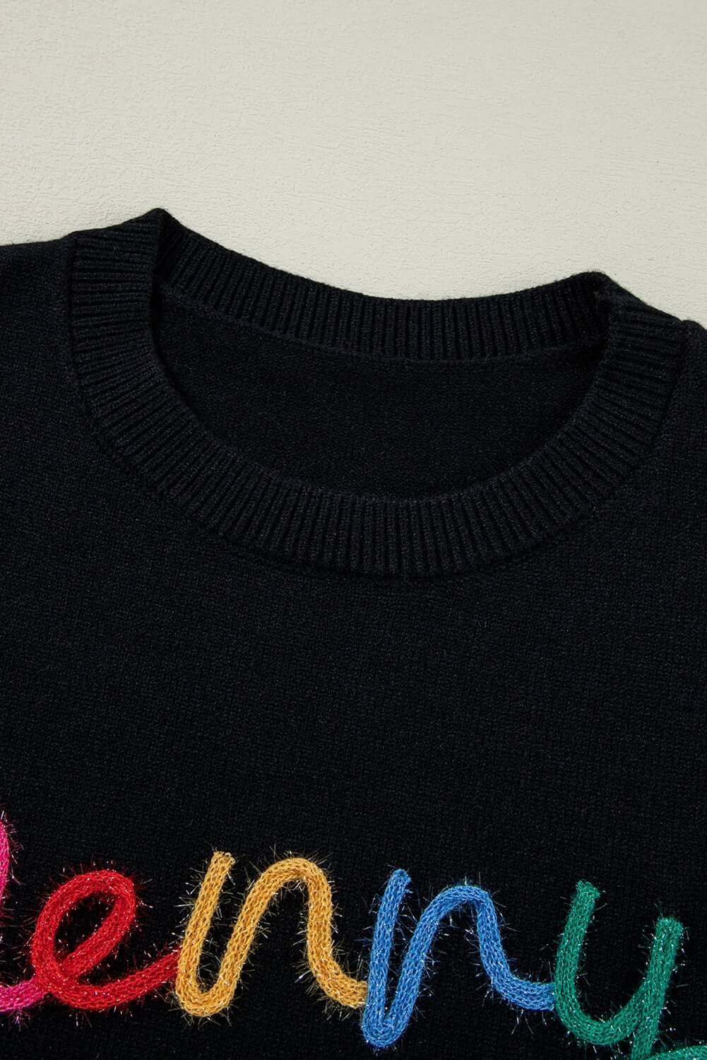 Close-up of MERRY & BRIGHT sweater by Vivian-Lu featuring colorful tinsel letters on a black background.