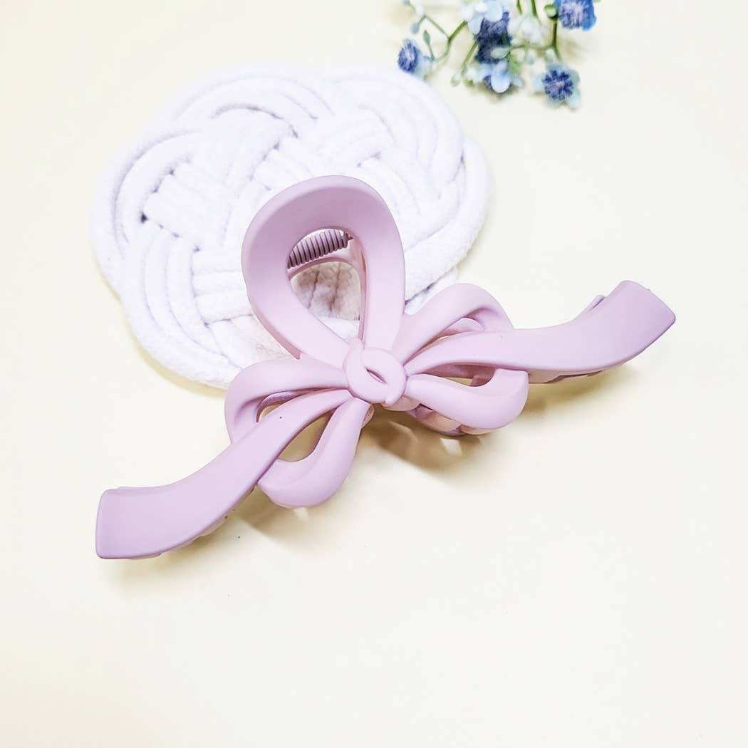 Matte lavender bow claw clip on a white braided hair accessory background.