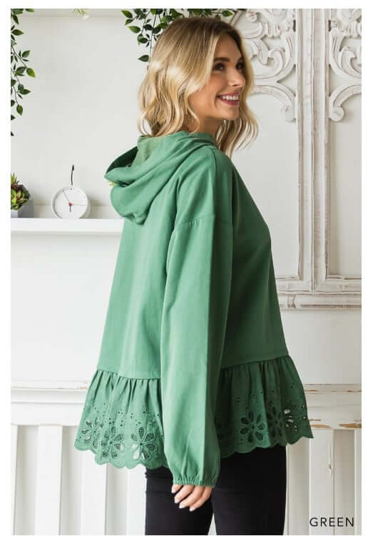 Woman wearing green ADVENTURE AWAITS hoodie with eyelet ruffle detail, showcasing a stylish oversized design.