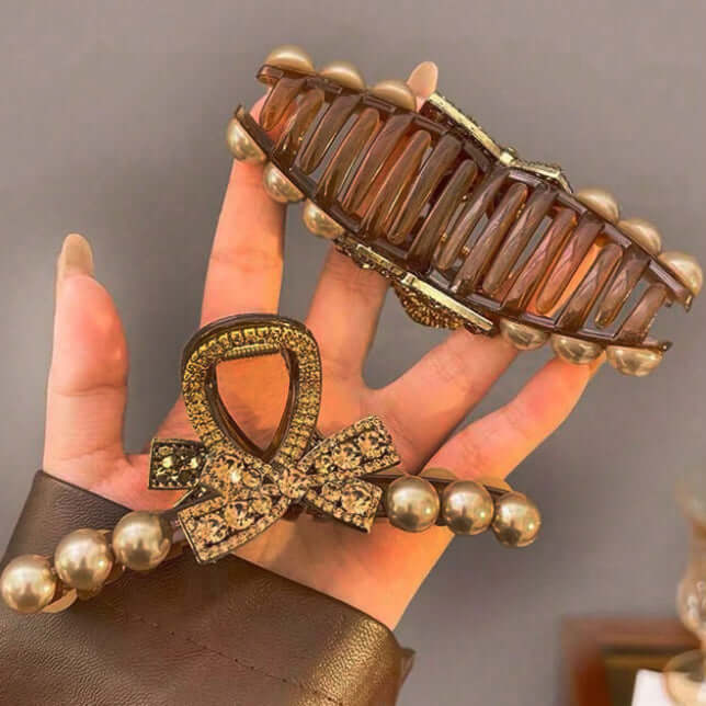 Champagne Chic hair clip featuring a rhinestone bow and dark rose gold pearls, held in a hand.