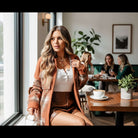 Model wearing HARVEST HAVEN JACKET in rust colorblock plaid, seated in a cafe with friends.