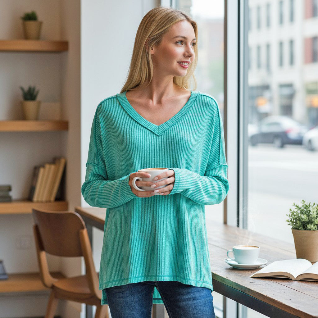 Woman wearing COZY CONCEPTS RIBBED TOP (turquoise) holding a coffee cup in a cozy café setting.