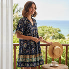 Model wearing the FINALLY MINE - UMGEE boho chic black mix floral mini dress on a balcony with a scenic view.