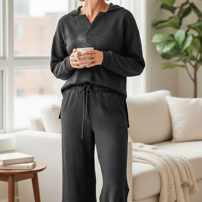 Woman in CALM & COLLECTED 2 PIECE SET, black textured lounge wear with a cozy vibe, holding a mug in modern living room.