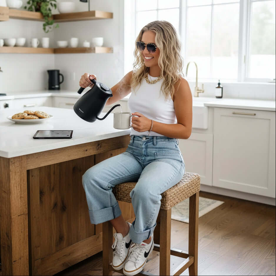 Woman in BLAKELY CLOVER FRONT POCKET JEANS pouring tea in a modern kitchen.