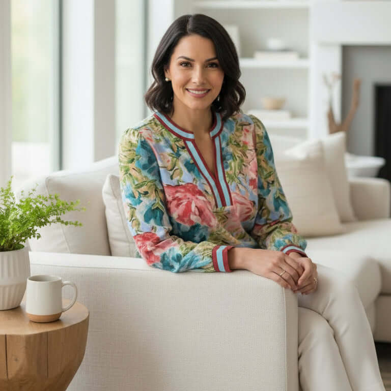 Woman wearing TEMPLATE TOP (long sleeve) blouse with floral print, styled elegantly in a modern living room.
