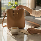 Polished Path Handbag (cinnamon) on table with coffee and notebook, showcasing its sleek design and premium vegan leather.